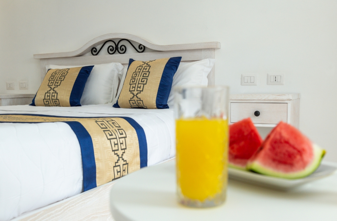 Camera elegante con letto, cuscini decorati, succo d'arancia e fette di anguria.