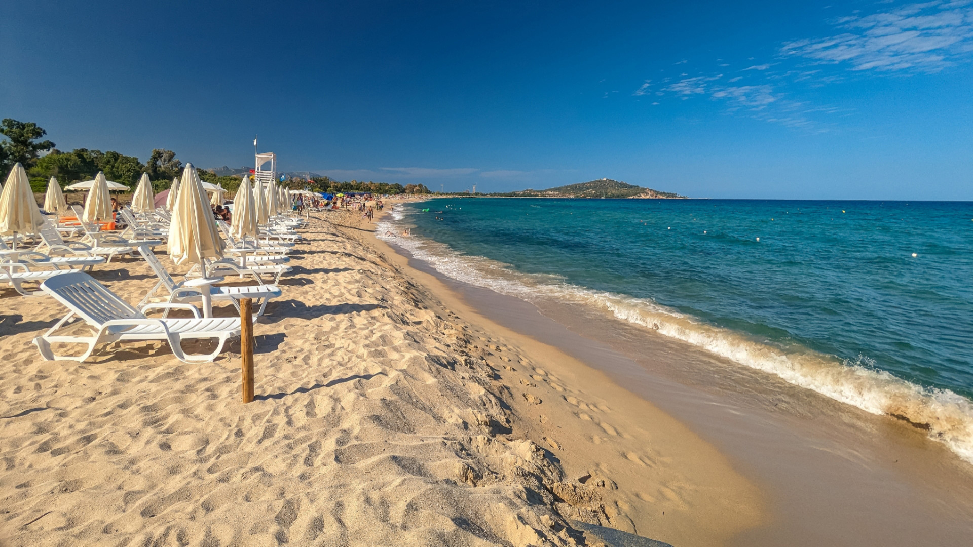 Spiaggia sabbiosa con lettini e ombrelloni bianchi, mare azzurro e cielo limpido.