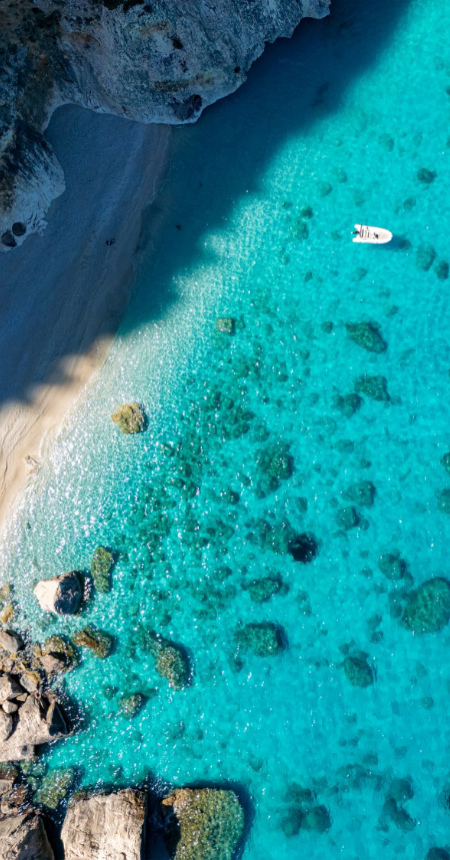 Spiaggia con acque turchesi e barche, vista dall'alto, circondata da scogliere rocciose.