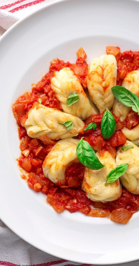 Gnocchi con sugo di pomodoro e basilico su piatto bianco.