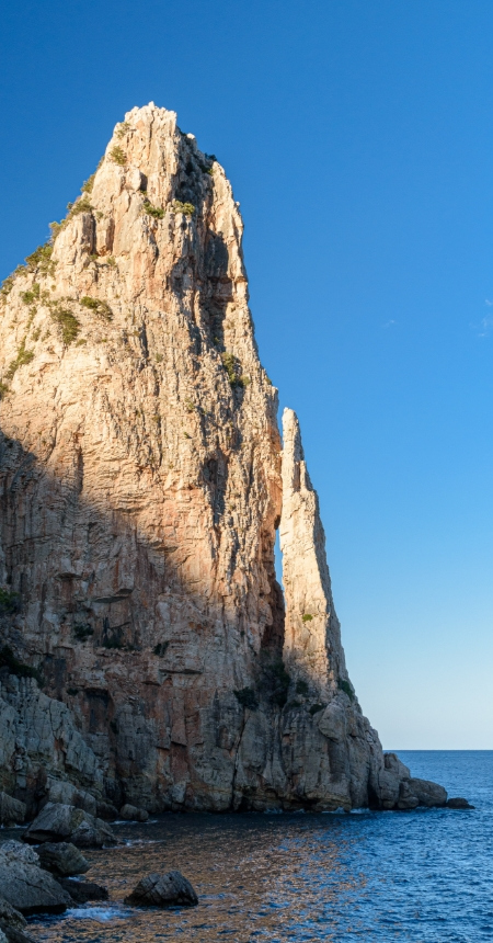 Imponente scogliera rocciosa si staglia contro il cielo azzurro e il mare.