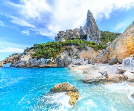 Spiaggia con mare cristallino e scogliere imponenti sotto un cielo azzurro.