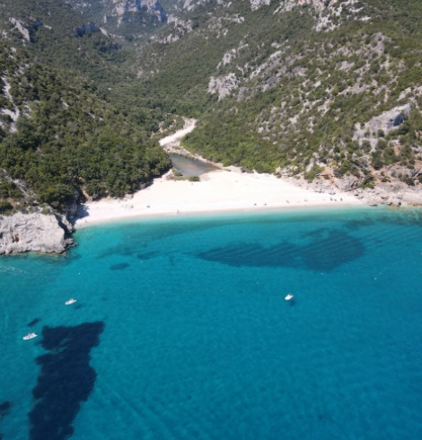 Spiaggia isolata con acque cristalline e barche, circondata da montagne verdi.