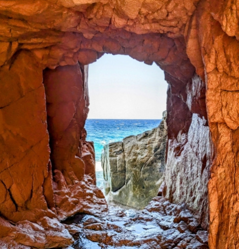 Vista sul mare attraverso una grotta di rocce rosse.