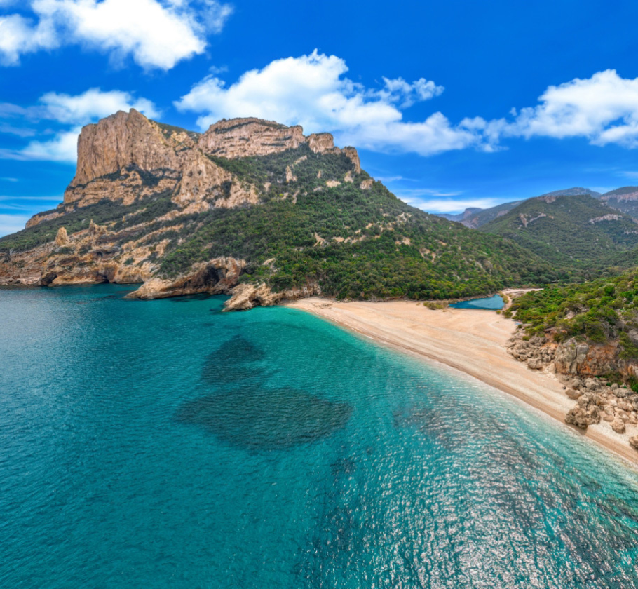 Spiaggia incontaminata con acque turchesi e montagne verdi sotto un cielo azzurro.