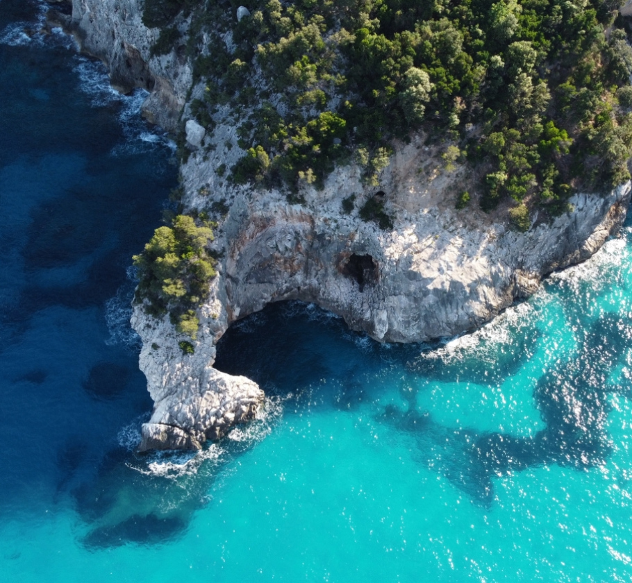 Costa rocciosa con archi naturali, mare cristallino e vegetazione rigogliosa.