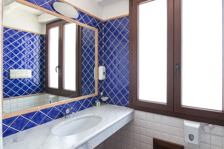 Bagno con piastrelle blu, lavabo in marmo e finestra grande.
